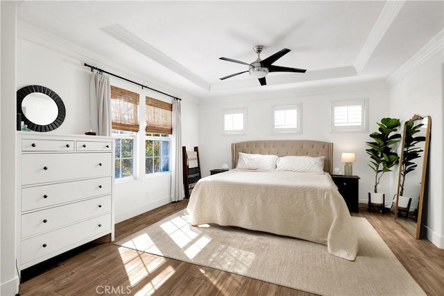 bedroom with a raised ceiling, ornamental molding, ceiling fan, wood finished floors, and baseboards