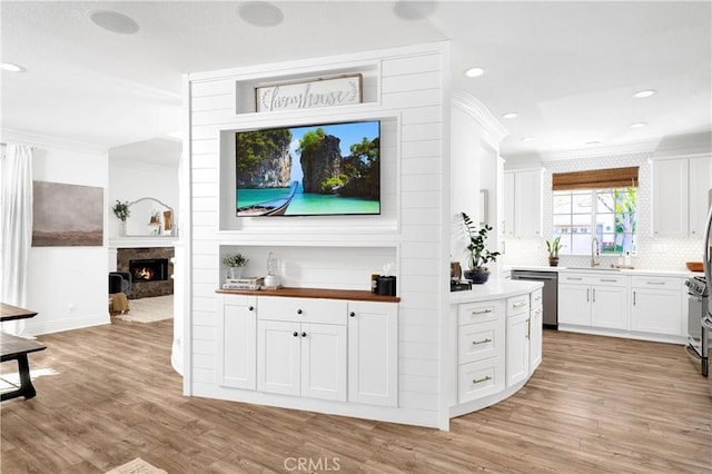 interior space with a warm lit fireplace, ornamental molding, light wood-type flooring, stainless steel dishwasher, and a sink