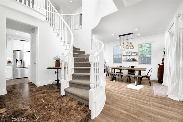 stairway with crown molding, recessed lighting, a high ceiling, wood finished floors, and baseboards