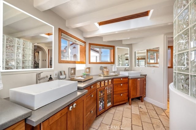 bathroom with double vanity, baseboards, a sink, and beamed ceiling