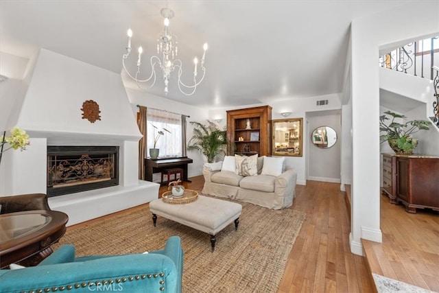 living room featuring light wood-style flooring, a notable chandelier, a fireplace, visible vents, and baseboards