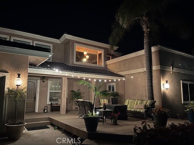 back of house at twilight with a wooden deck, an outdoor living space, and stucco siding