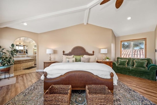 bedroom featuring lofted ceiling with beams, ensuite bath, arched walkways, and wood finished floors