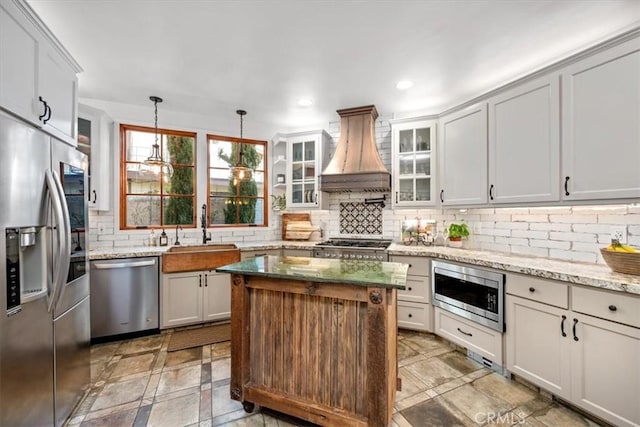 kitchen with tasteful backsplash, recessed lighting, appliances with stainless steel finishes, a sink, and premium range hood