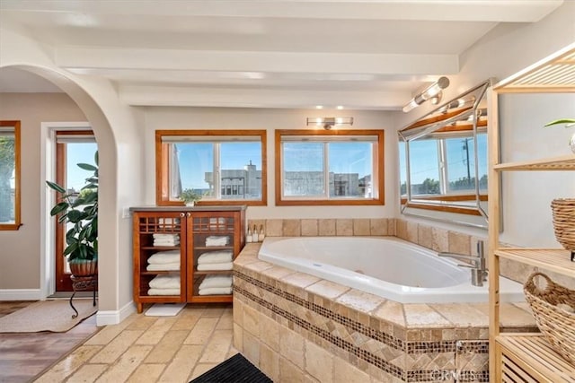 bathroom featuring beamed ceiling, a bath, and baseboards