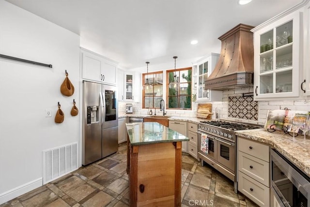 kitchen featuring visible vents, decorative backsplash, appliances with stainless steel finishes, light stone countertops, and custom exhaust hood