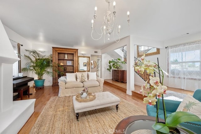 living room with light wood-type flooring, visible vents, stairway, and an inviting chandelier