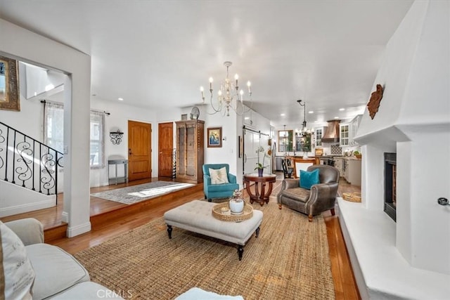 living area featuring a chandelier, wood finished floors, a fireplace with raised hearth, and stairs