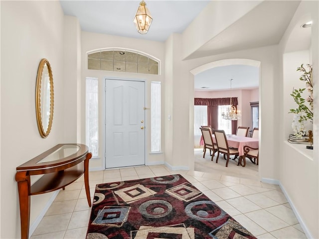 entryway with light tile patterned floors, a notable chandelier, arched walkways, and baseboards