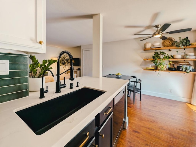 kitchen with light stone counters, light wood finished floors, stainless steel dishwasher, a ceiling fan, and a sink