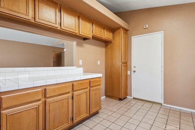 kitchen with light tile patterned floors, tile countertops, brown cabinetry, and baseboards