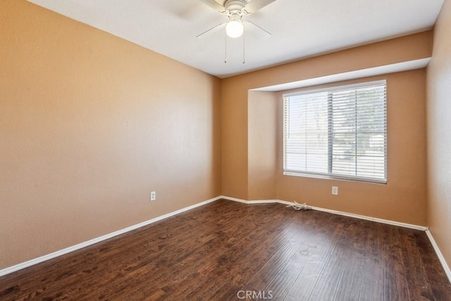 spare room with dark wood-style flooring, a ceiling fan, and baseboards