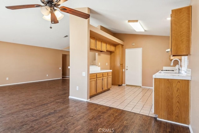 kitchen with visible vents, tile counters, light wood-style flooring, vaulted ceiling, and a sink