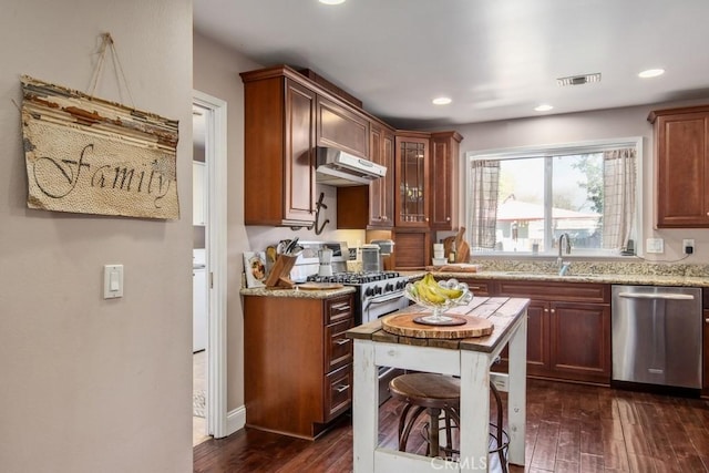 kitchen with stainless steel appliances, dark wood-type flooring, a sink, light stone countertops, and under cabinet range hood