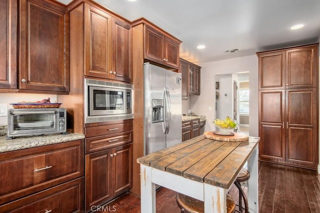 kitchen with stainless steel appliances, a toaster, dark wood-type flooring, and light stone counters