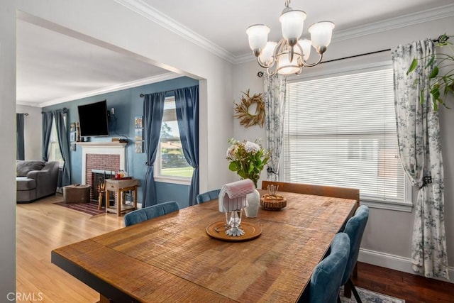 dining room with ornamental molding, a brick fireplace, a notable chandelier, and wood finished floors