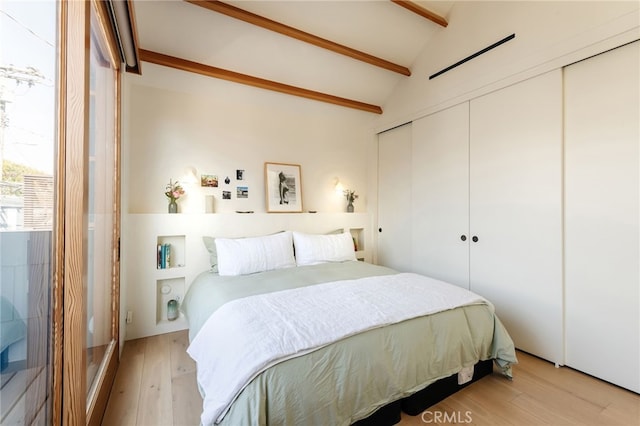 bedroom with light wood-type flooring, a closet, and lofted ceiling with beams