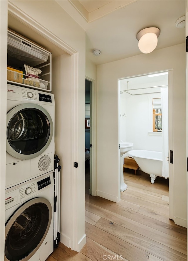 clothes washing area with laundry area, light wood-style flooring, and stacked washer and clothes dryer