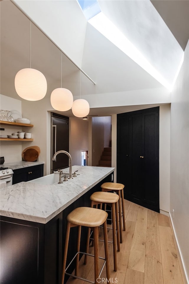 kitchen with light stone counters, a sink, a kitchen breakfast bar, baseboards, and light wood-style floors