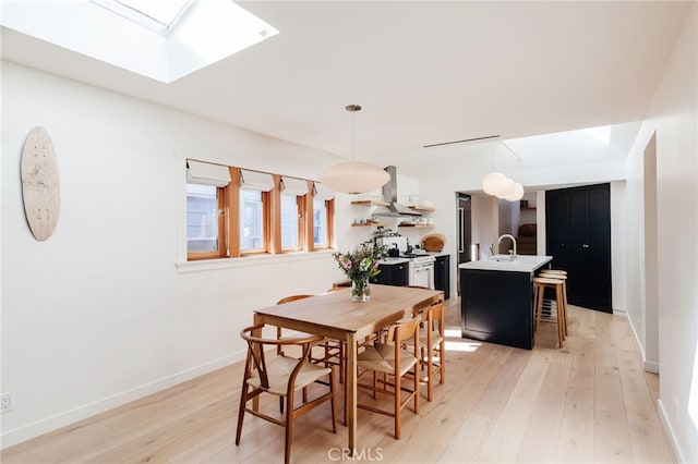 dining space featuring light wood-style floors, a skylight, and baseboards