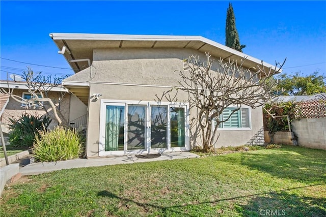 rear view of property with a lawn, fence, and stucco siding