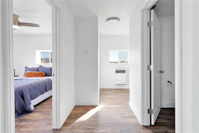 hallway with baseboards, wood finished floors, and heating unit