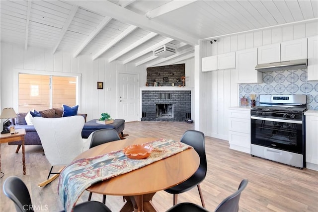 dining area with light wood-type flooring, a brick fireplace, a wall mounted air conditioner, and lofted ceiling with beams