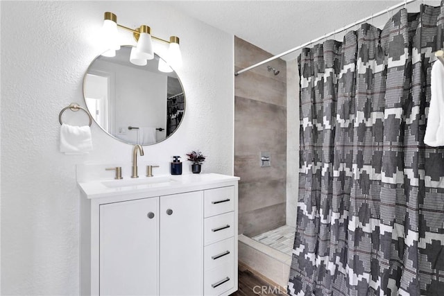 full bath featuring a textured wall, a tile shower, and vanity