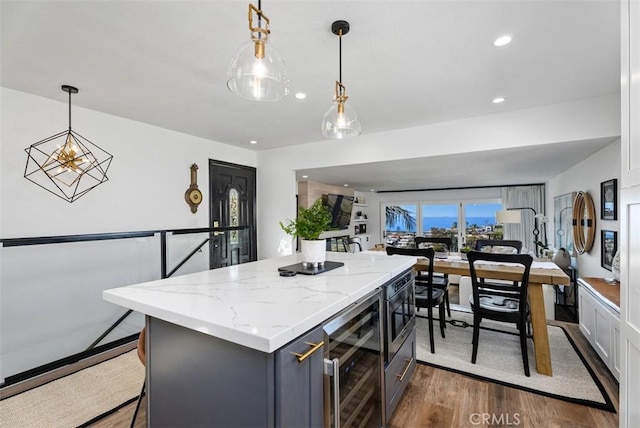 kitchen featuring beverage cooler, dark wood-style floors, a kitchen island, light stone counters, and hanging light fixtures