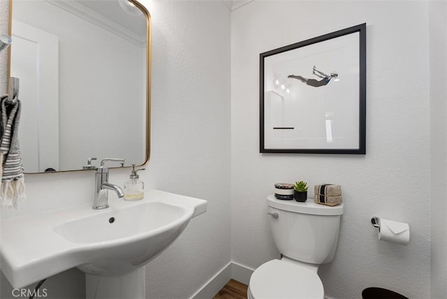 bathroom with toilet, ornamental molding, a sink, wood finished floors, and baseboards