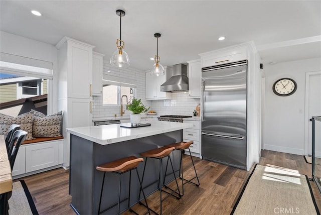 kitchen with dark wood-style flooring, stainless steel built in fridge, wall chimney range hood, and white cabinets