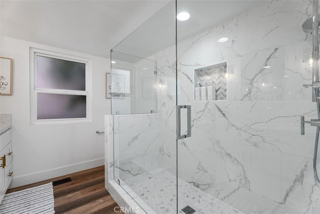 bathroom featuring a marble finish shower, baseboards, wood finished floors, vanity, and recessed lighting