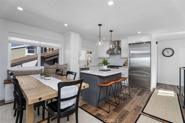 kitchen featuring wall chimney exhaust hood, backsplash, built in fridge, and white cabinets