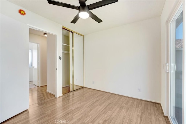 unfurnished bedroom featuring multiple windows, light wood-type flooring, a closet, and a ceiling fan