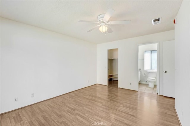 unfurnished bedroom with a walk in closet, visible vents, light wood-style flooring, a ceiling fan, and connected bathroom