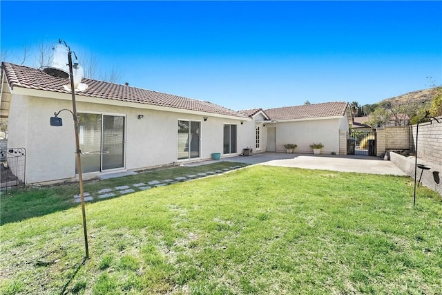 rear view of house featuring a lawn, a patio, a tile roof, fence, and stucco siding