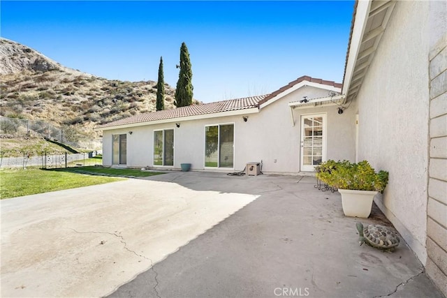 back of house featuring a lawn, a patio, a tiled roof, fence, and stucco siding