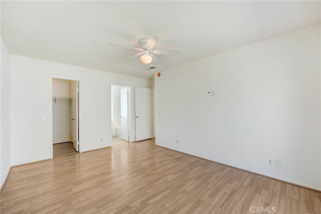 unfurnished bedroom featuring ceiling fan, light wood-style floors, a closet, a walk in closet, and ensuite bath