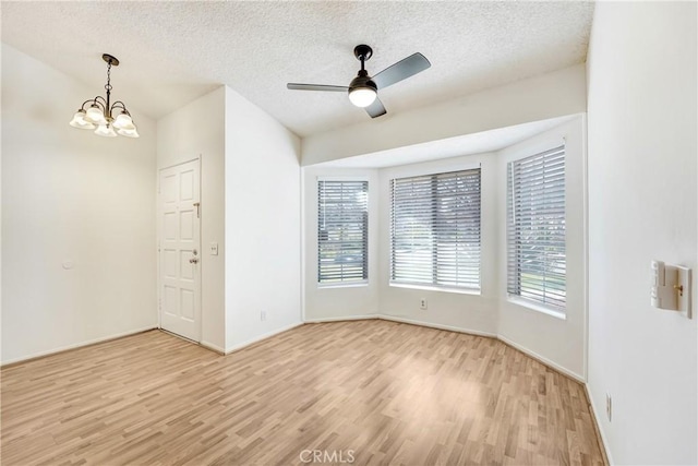 spare room featuring light wood-style floors, a textured ceiling, baseboards, and ceiling fan with notable chandelier