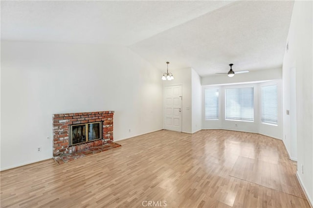 unfurnished living room featuring a brick fireplace, vaulted ceiling, light wood finished floors, and ceiling fan with notable chandelier