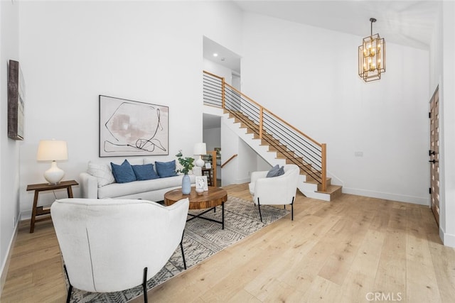 living area featuring a high ceiling, an inviting chandelier, wood finished floors, baseboards, and stairs