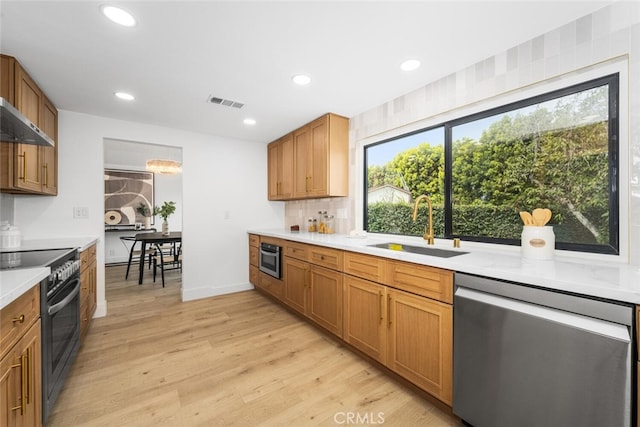 kitchen featuring range with electric cooktop, a sink, light countertops, dishwasher, and light wood finished floors