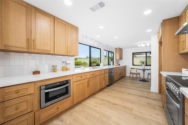 kitchen featuring light wood-style flooring, stainless steel appliances, a sink, visible vents, and decorative backsplash