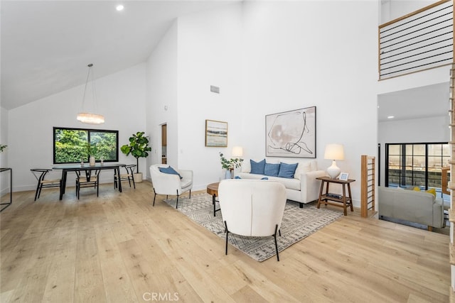 living room with baseboards, high vaulted ceiling, light wood-type flooring, and an inviting chandelier