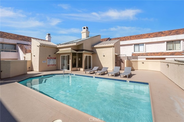 rear view of house with a patio, stucco siding, a standing seam roof, metal roof, and a community pool