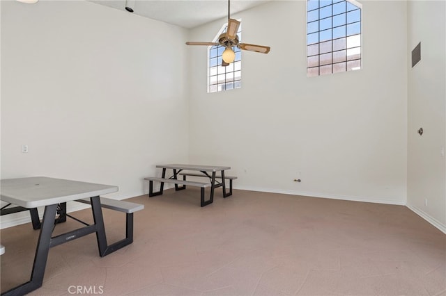 interior space with ceiling fan, a high ceiling, light colored carpet, and baseboards