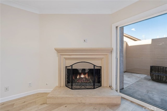 interior details featuring crown molding, a lit fireplace, baseboards, and wood finished floors