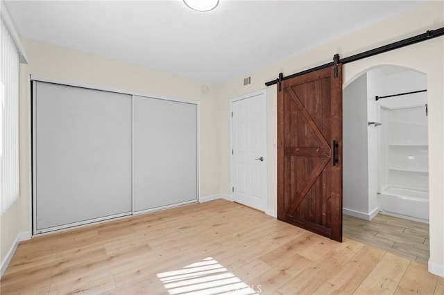 unfurnished bedroom with a barn door, baseboards, visible vents, light wood-style flooring, and a closet