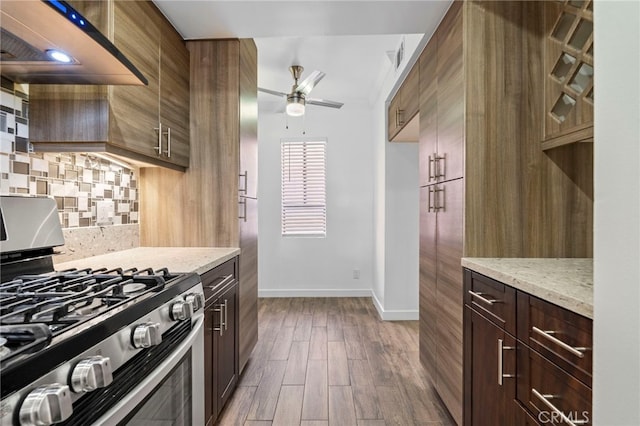 kitchen with ceiling fan, ventilation hood, stainless steel range with gas cooktop, decorative backsplash, and dark wood finished floors