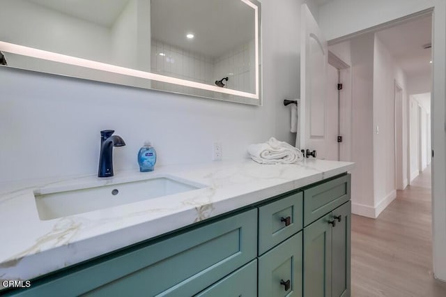 bathroom with recessed lighting, wood finished floors, a sink, tiled shower, and double vanity